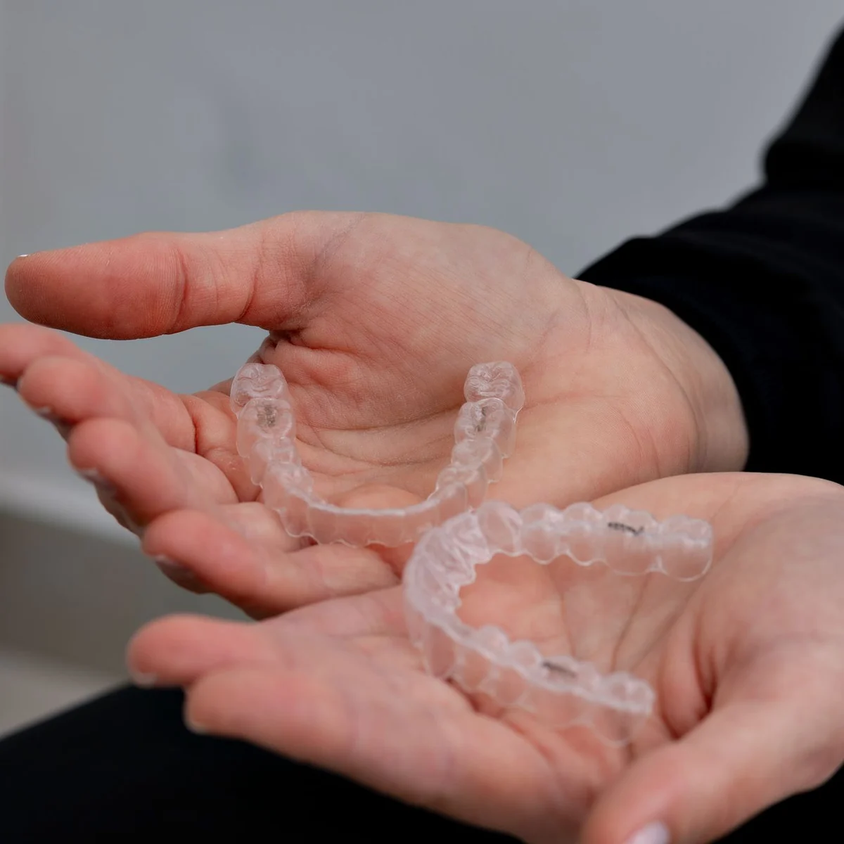 Dłonie trzymające przezroczyste nakładki Invisalign na górny i dolny łuk